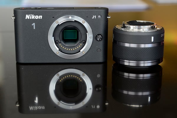 Nikon 1 Nikon 1 J1 camera with lens detached and reflected on surface.